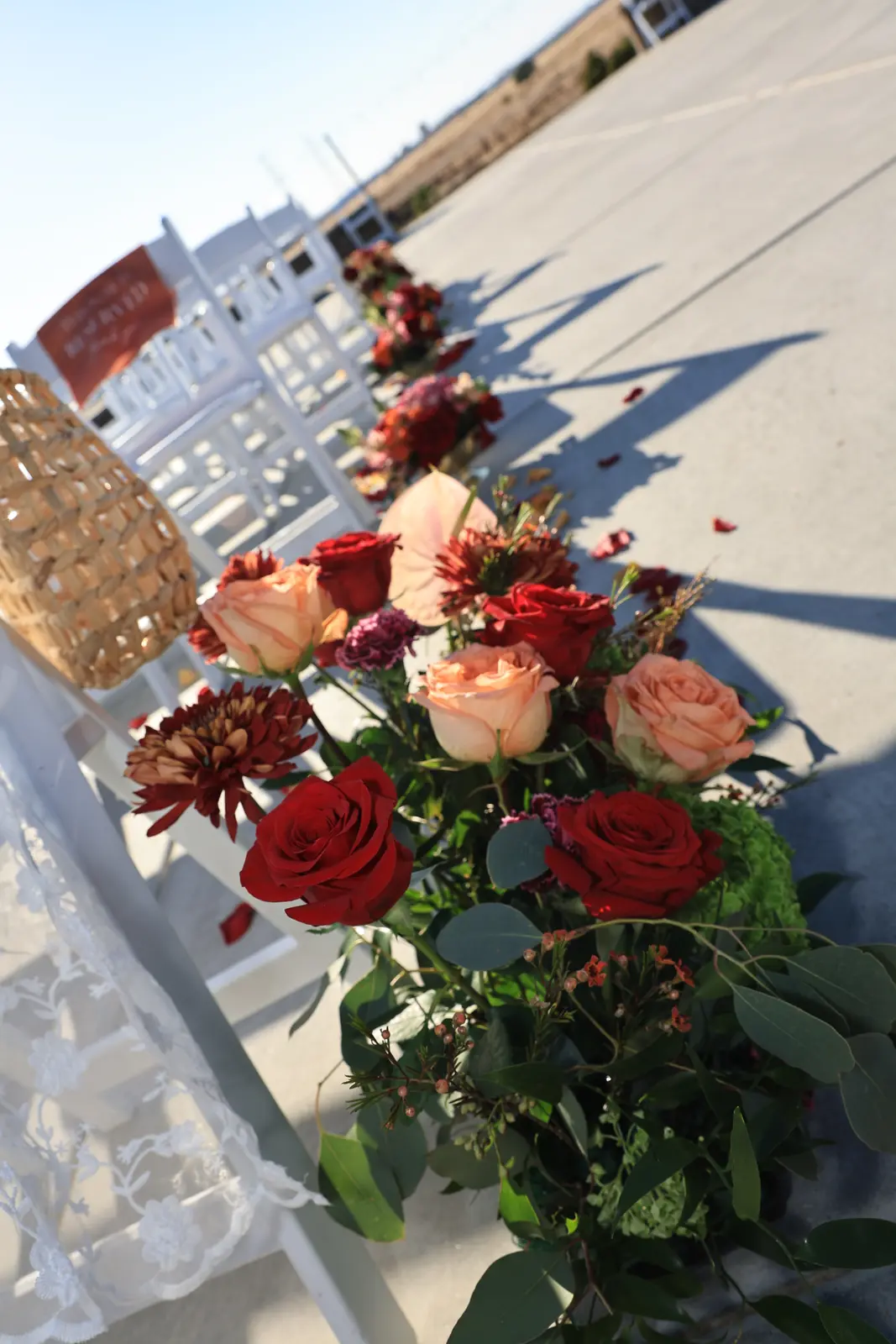 Red, peach, and coral rose aisle arrangement beside white ceremony chairs