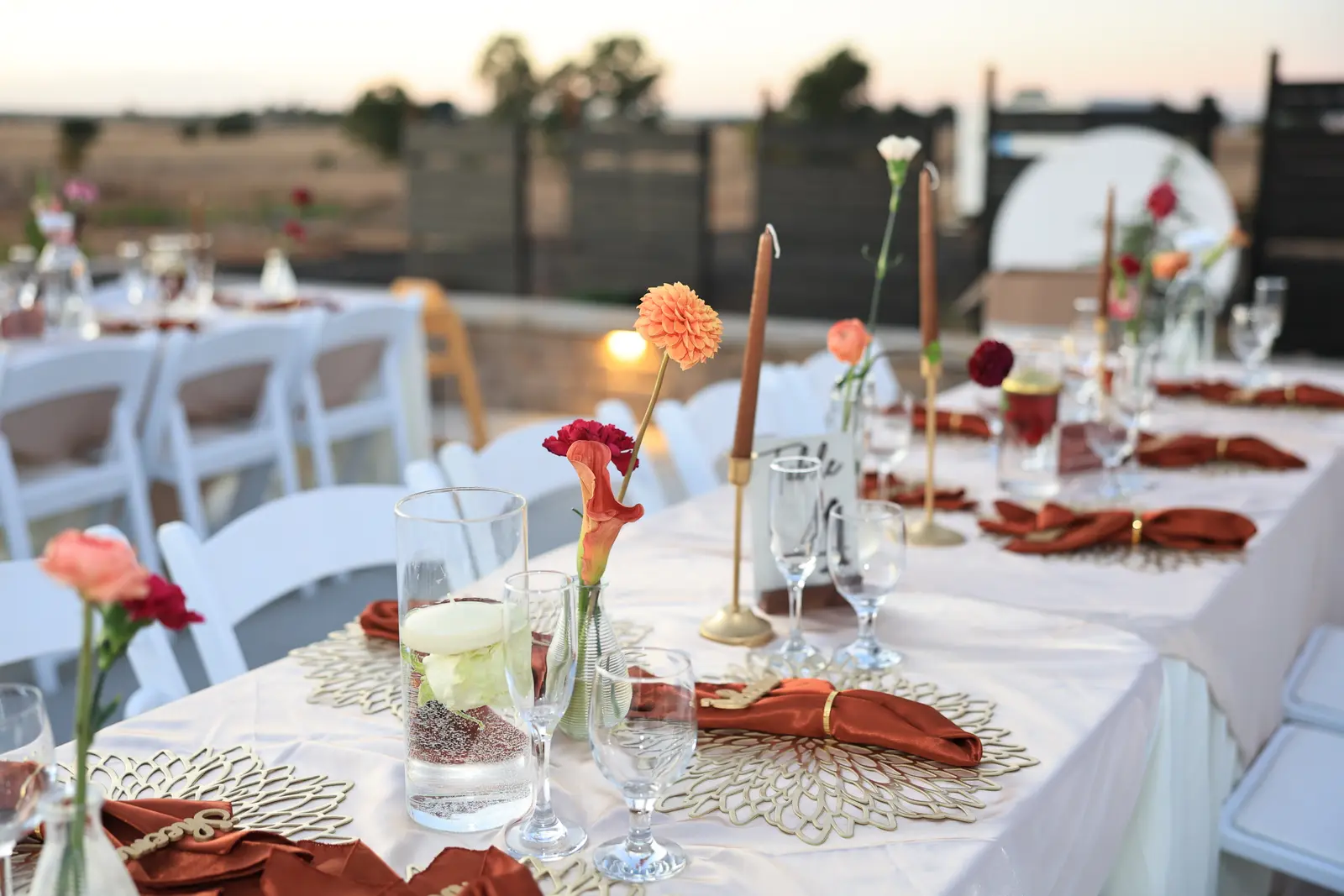 Bud vases of dahlias and roses between taper candles on the reception table