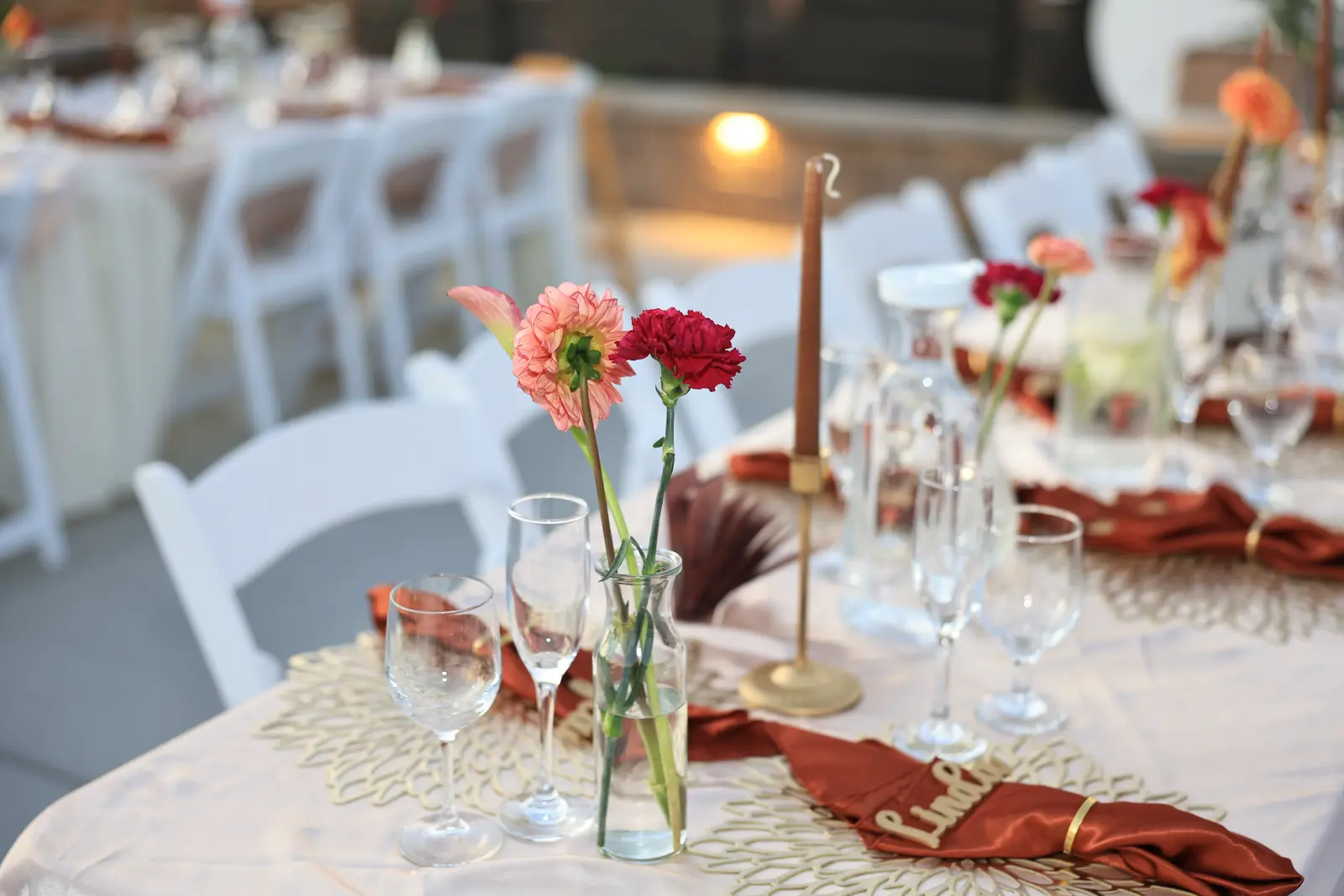 Single dahlia bud vase and glassware at a reception place setting