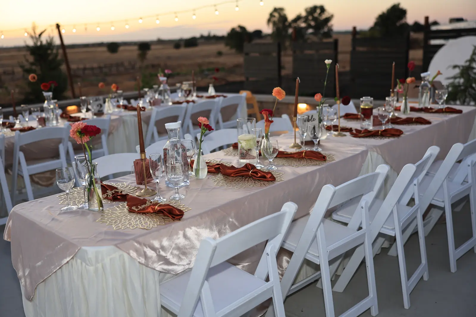 Reception long tables set with bud vases and rust napkins at sunset