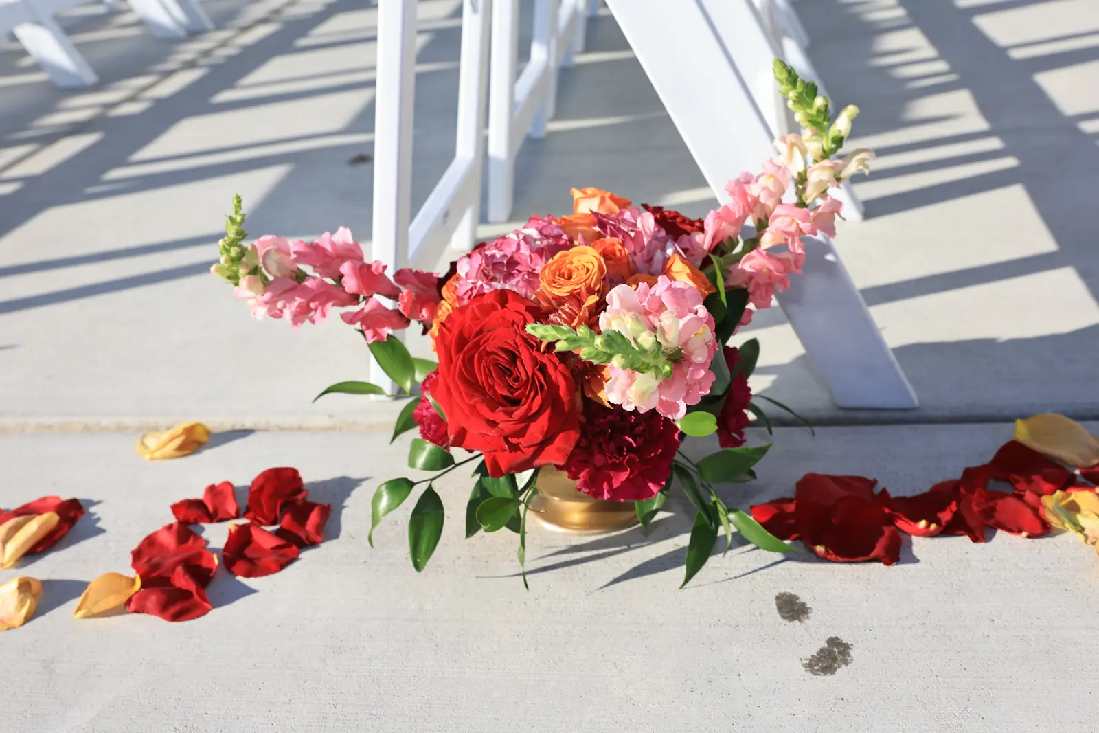 Pink snapdragon and red rose aisle arrangement scattered with petals