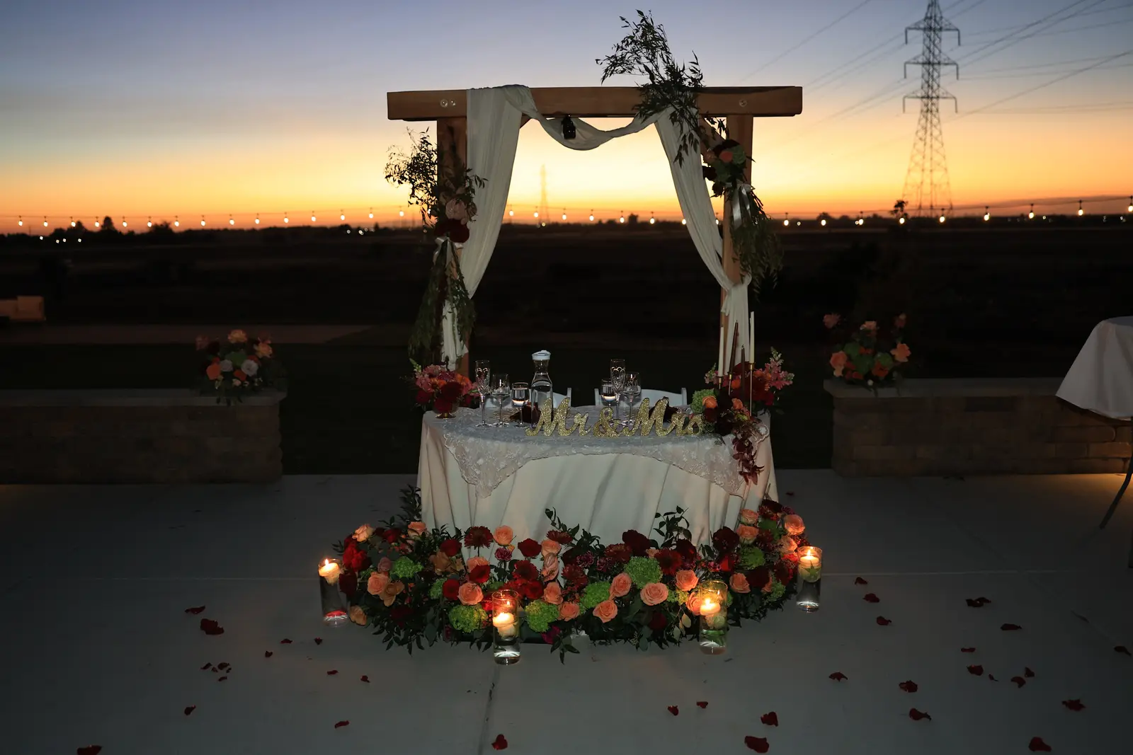 Draped wooden arch over the sweetheart table against a sunset sky