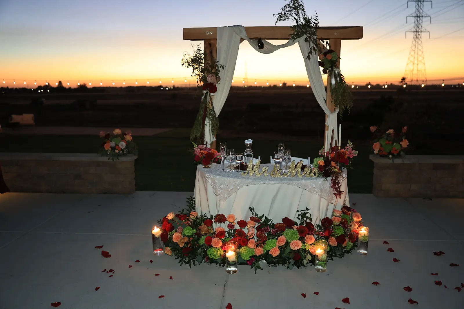 Sweetheart table ringed in red and coral roses and candlelight at dusk